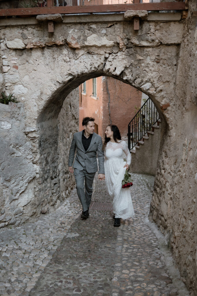 Couple walking through an old stone archway during their Malcesine elopement on Lake Garda