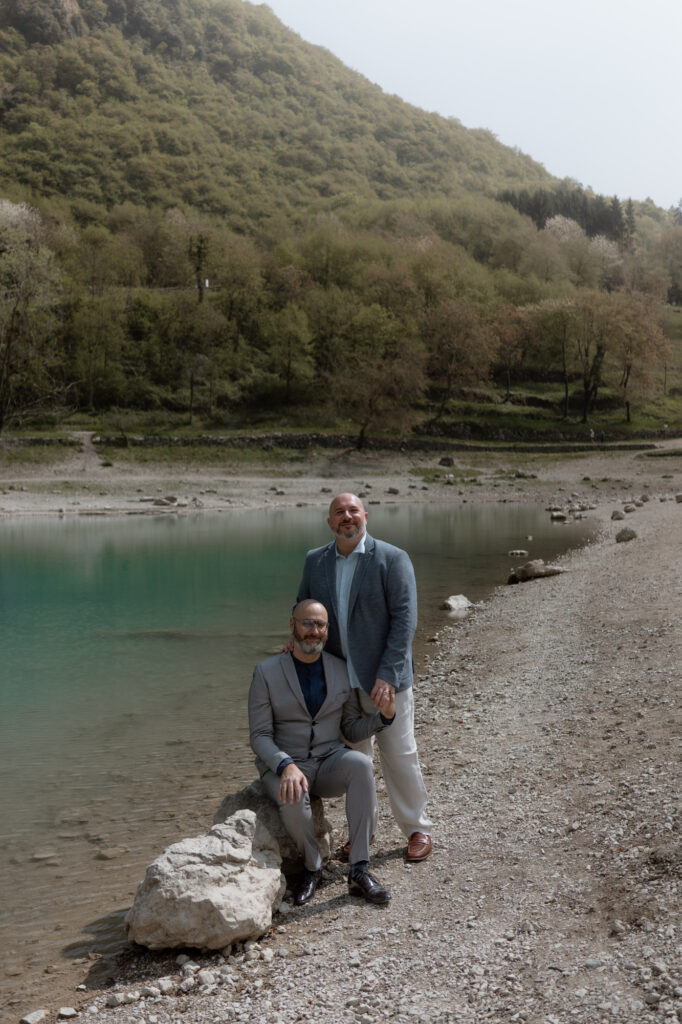 LGBTQ+ couple posing by the turquoise water of Lake Tenno during their elopement in Italy