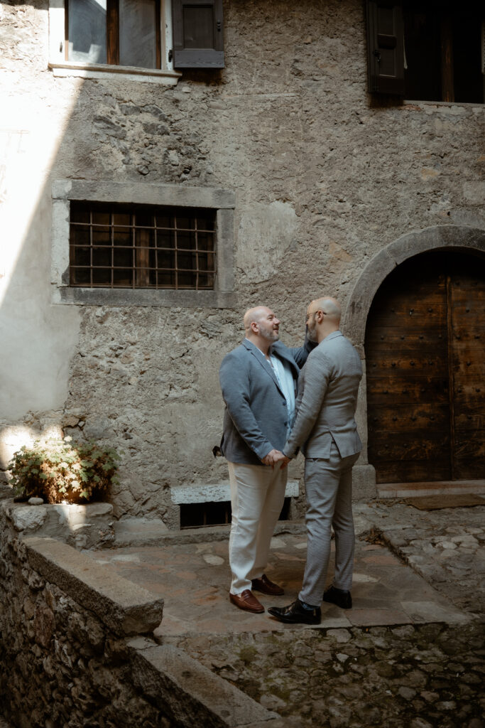 LGBTQ+ couple holding hands in a stone village near Lake Tenno during their Italy elopement