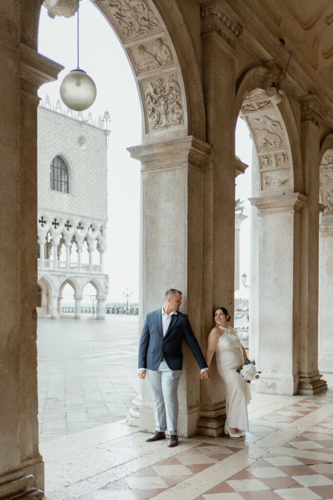 Couple holding hands under historic arches during their Venice elopement in Italy